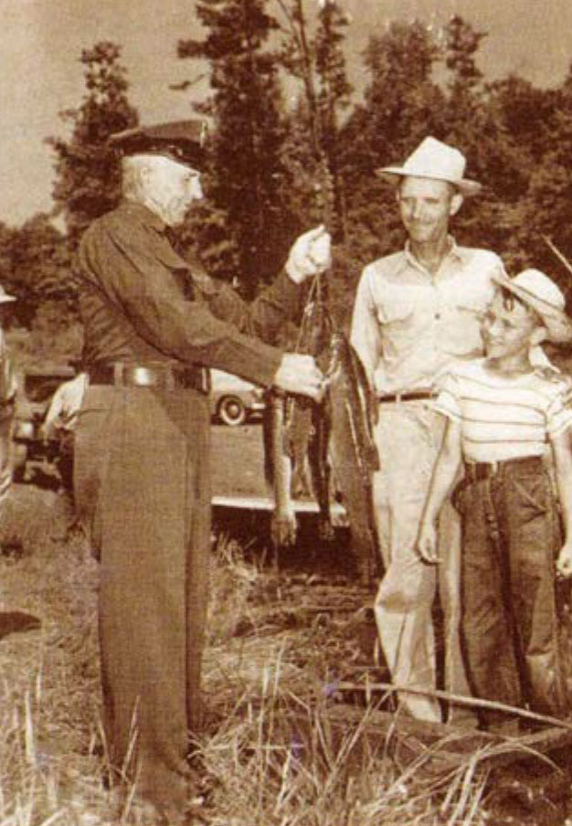 Isang itim at puting imahe ng isang game warden na may hawak na isda na nakikipag-usap sa dalawang tao