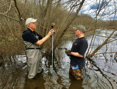 Isang imahe ng dalawang empleyado ng clover power station na naglalagay ng nesting box sa isang stand sa isang ilog