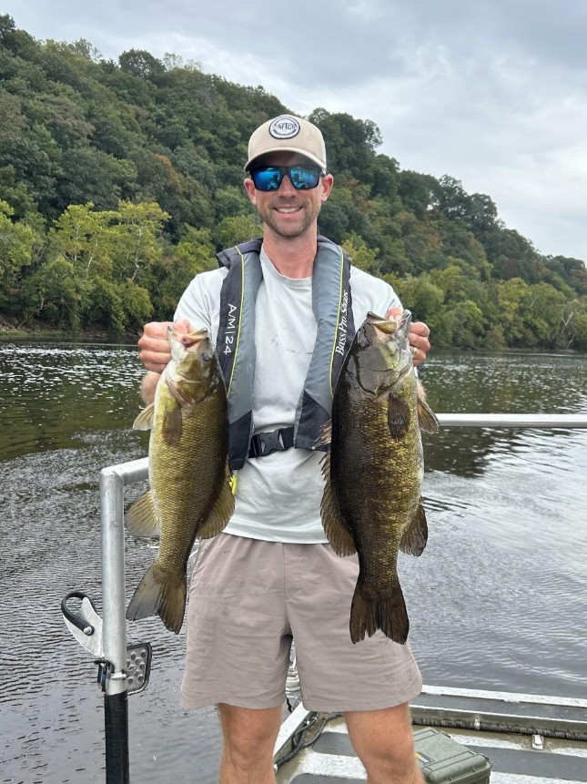 Mangingisda na nakatayo sa isang bangka at may hawak na dalawang smallmouth bass sa Upper James River.