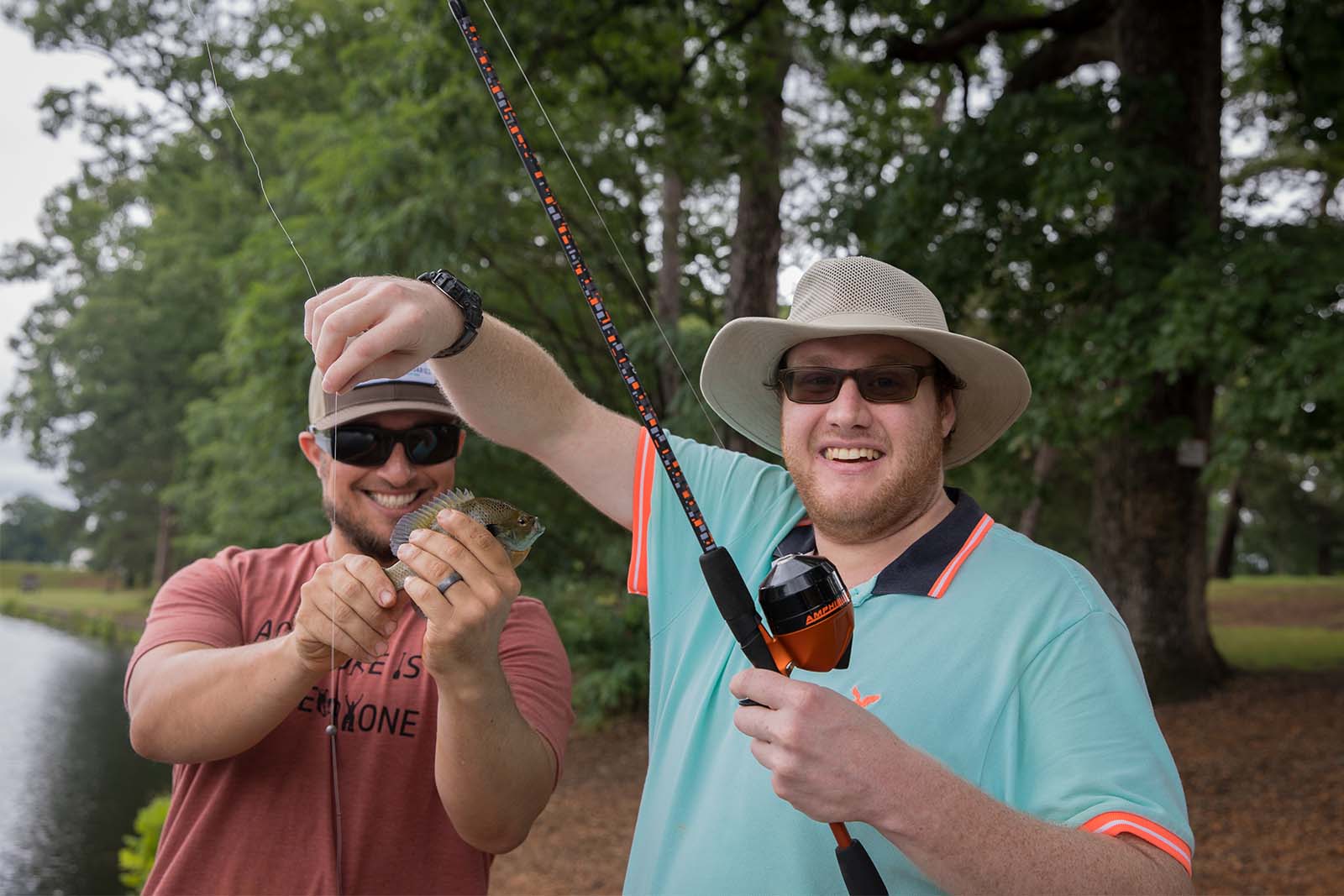 Dalawang lalaking nakatayo sa baybayin ng isang lawa. Ang isang tao ay may hawak na pamingwit habang ang isa naman ay may hawak na isda na natanggal sa kawit