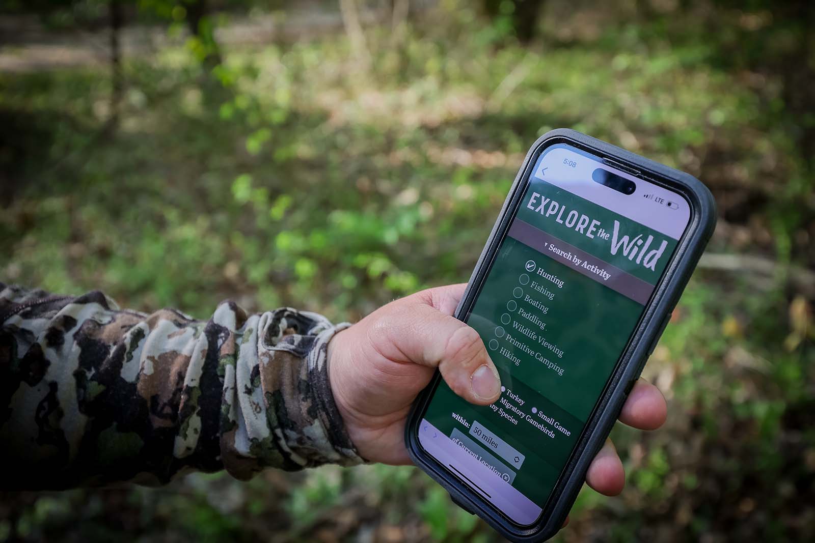 Isang kamay na may hawak na smartphone na may ipinapakitang Explore the Wild