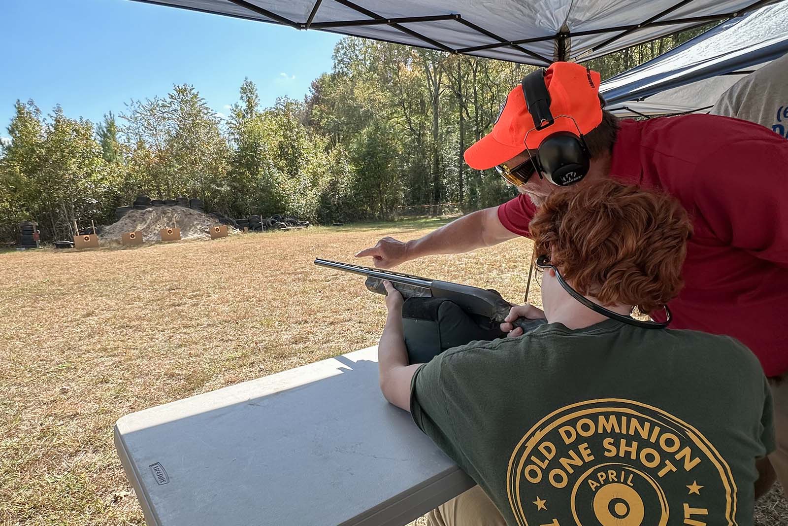 Isang taong nagsasanay sa pagbaril ng mga target gamit ang isang shotgun; isang instructor ang nakatayo malapit na nakaturo sa target