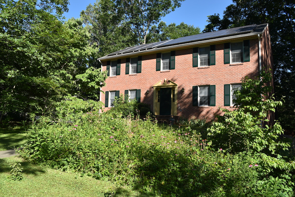 Isang imahe ng isang brick house na may mga solar panel sa bubong at isang pollinator garden sa harap ng bakuran