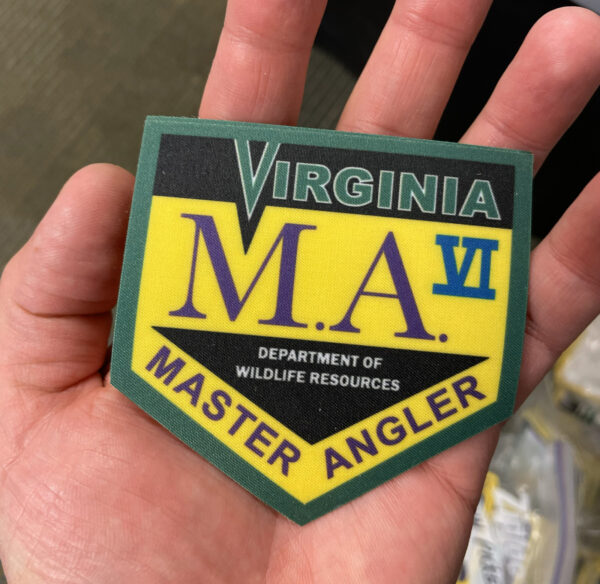 Isang larawan ng isang kamay na may hawak na isang iron-on patch na may Virginia Master Angler VI na nakasulat dito.