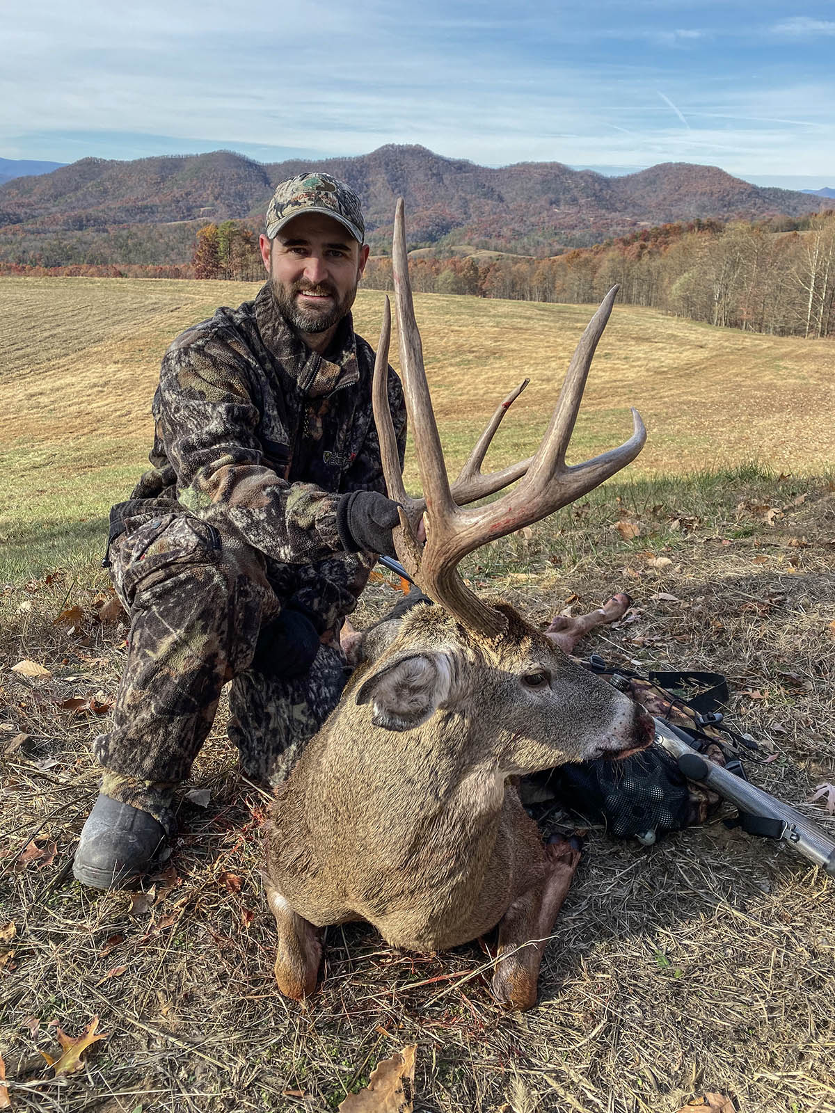 Isang mangangaso na nakasuot ng camouflage na nagpose na may malaking puting-tailed deer buck na may malalaking sungay.