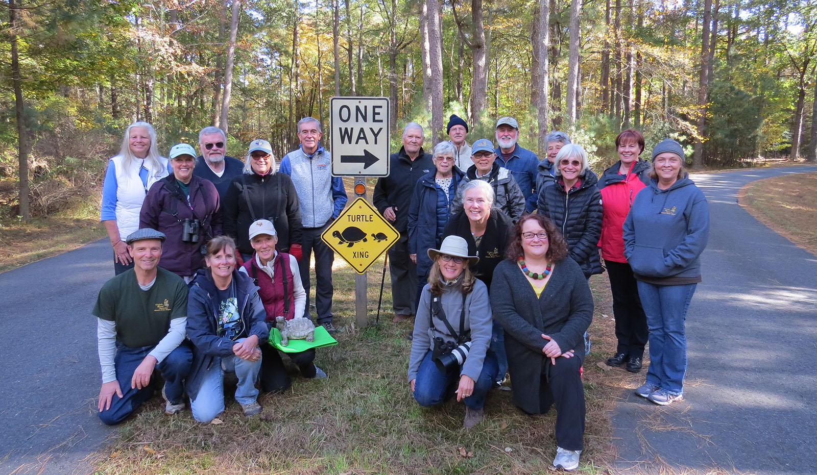 Isang grupo ng 20 mga tao ang nagtipun-tipon sa paligid ng isang karatula na tumatawid sa pagong sa gitna ng isang maliit na sementadong kalsada, na may isang tao na nakaluhod sa harapan na may estatwa ng pagong.
