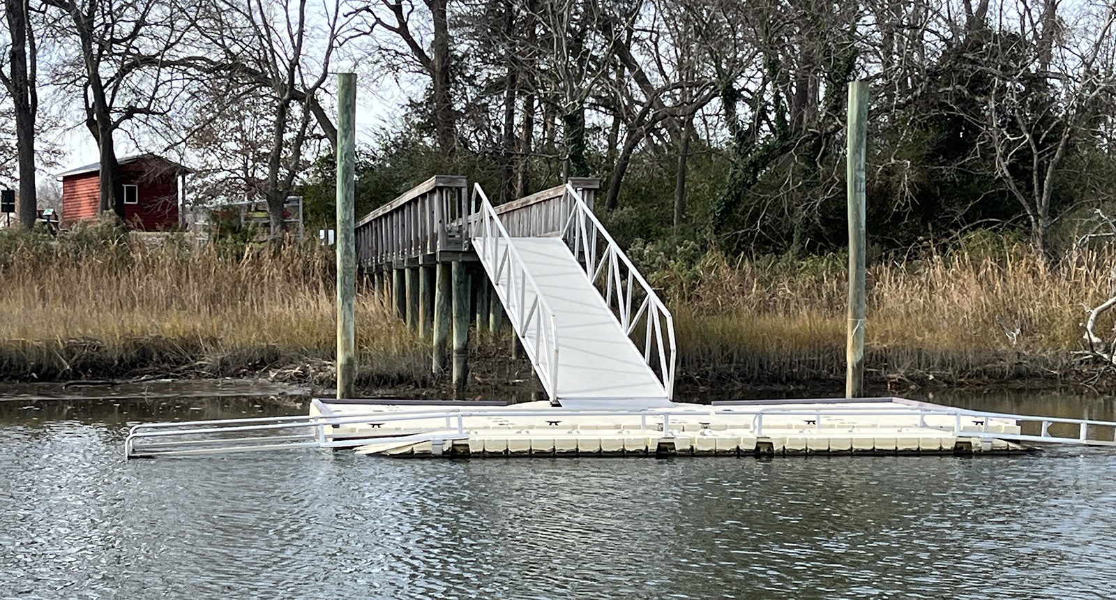 Isang larawan ng isang aluminum kayak launch na nakausli sa tubig ng isang ilog mula sa pampang.