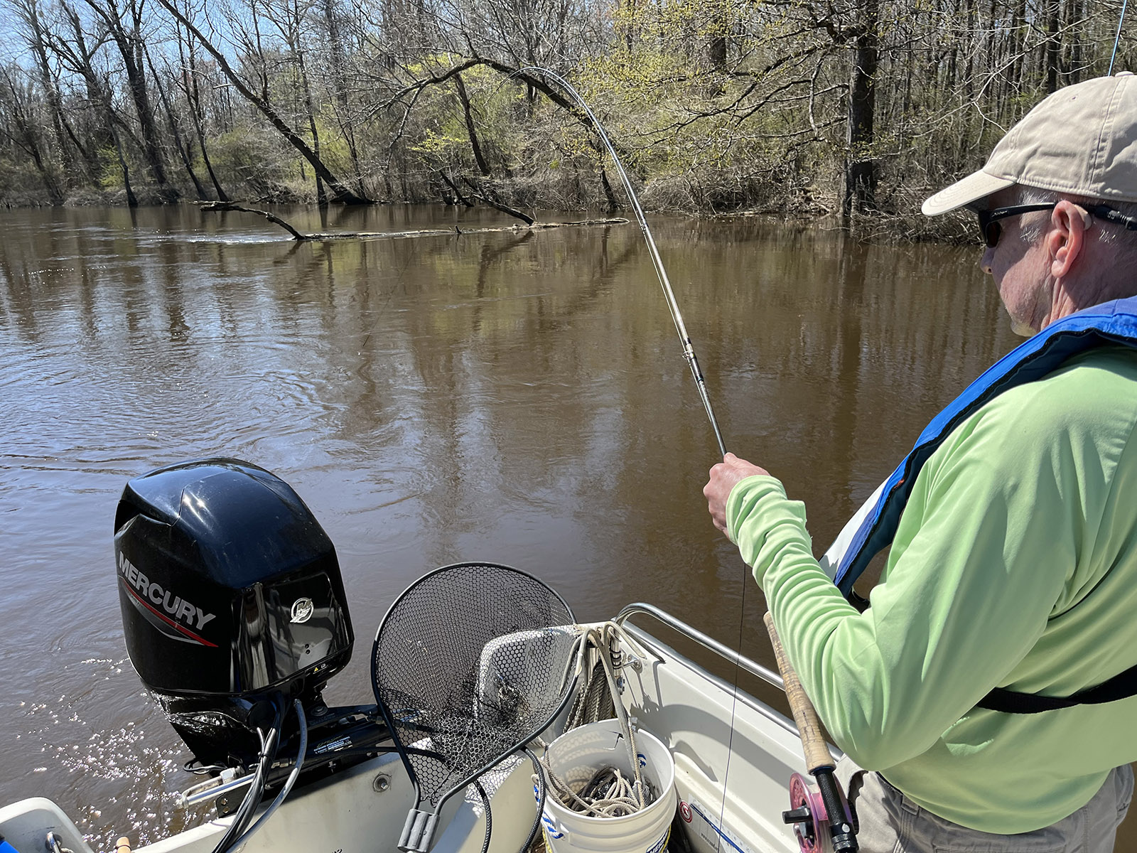 Larawan ng isang lalaking nakatayo sa isang bangka na may fly fishing rod na nakayuko sa tubig.