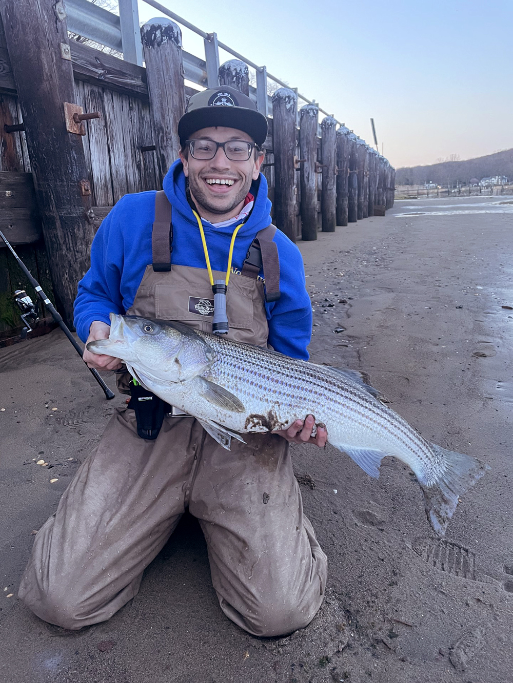 Isang imahe ni Josh McGilly sa isang beach na may hawak na malaking striped bass