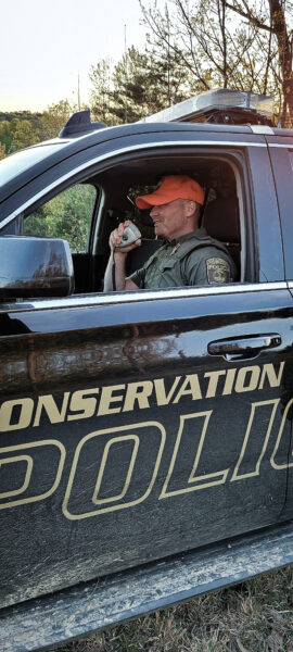 Isang imahe ng isang DWR conservation police officer na nakikipag-usap sa kanyang walkie talkie sa loob ng kanyang sasakyan 
