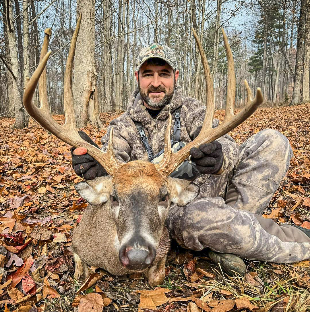 Isang larawan ng isang lalaking naka-camouflage at isang malaking whitetail deer buck.