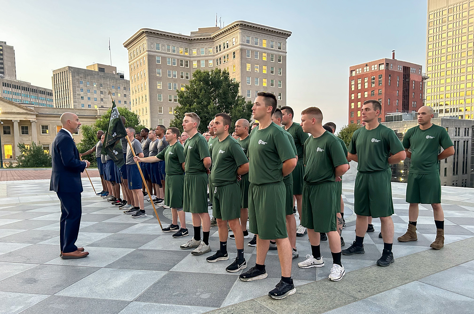 Isang grupo ng mga kabataang lalaki at babae na nakatayo sa atensyon na tinutugunan ng isang lalaking naka-suit habang nakatayo sa hagdan ng gusali ng Virginia Capitol.