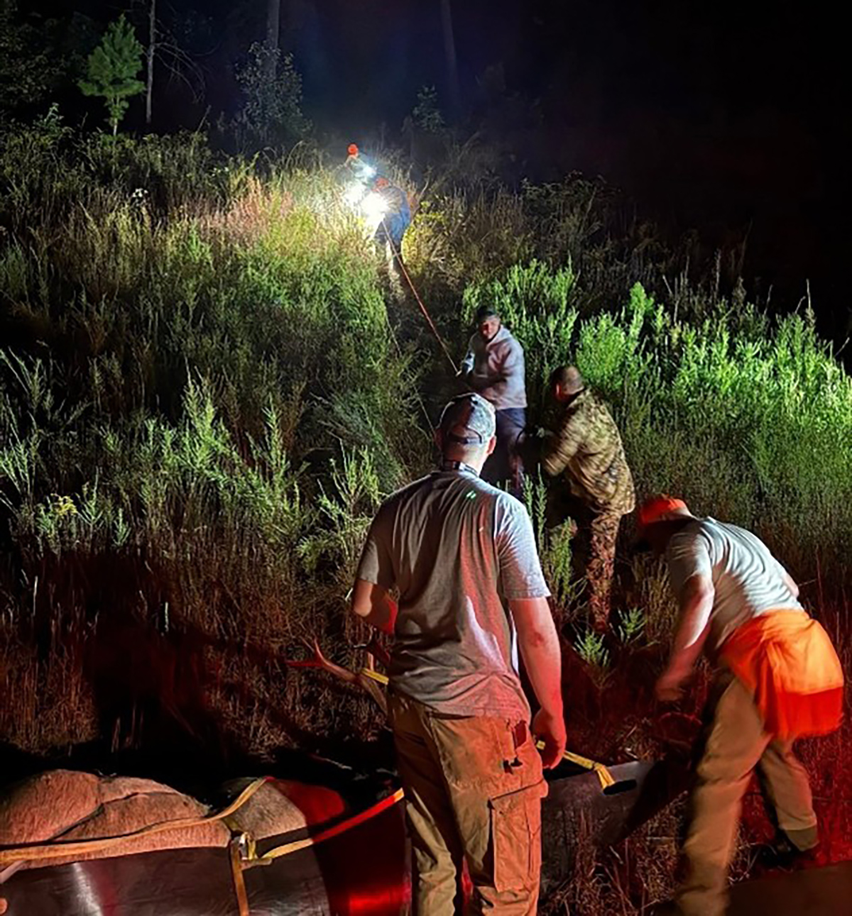 Isang larawan na kuha sa gabi ng mga kalalakihan na may headlamp sa pagbaba ng isang elk sa isang sled pababa sa matarik na burol.