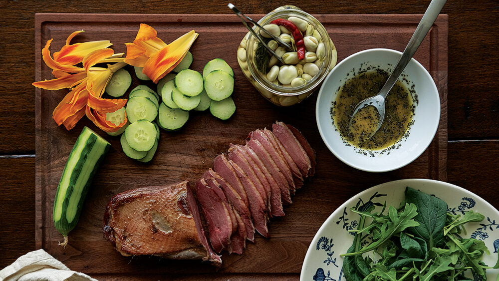 Isang larawan ng isang serving ng Pinausukang gansa, day lilies, cucumber, arugula, at adobo na fava beans