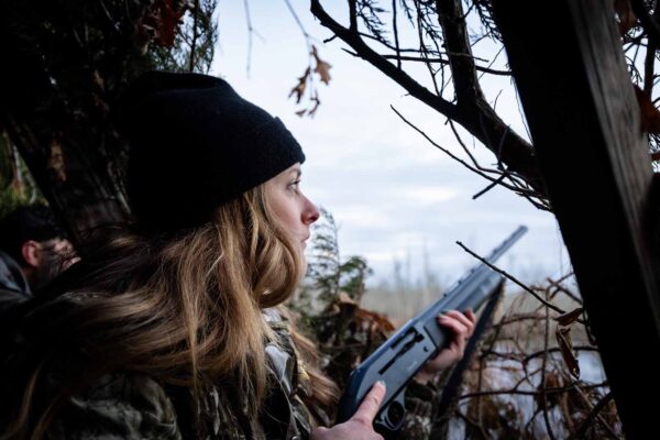 Isang babaeng nakasuot ng camouflage sa isang hunting blind sa tabi ng tubig