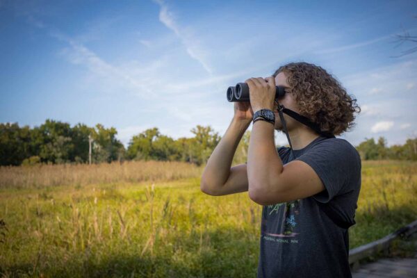 Isang lalaking naka t-shirt na may hawak na binocular at nakatingin sa malayo