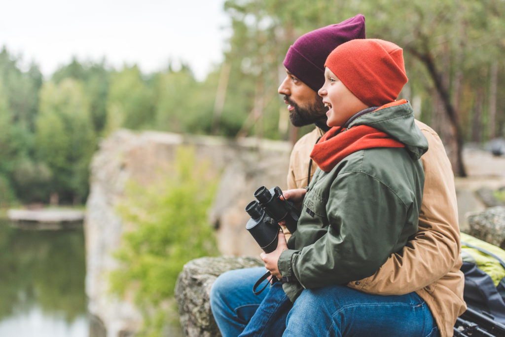 Nakatingin sa kaliwa ang larawan ng lalaking may hawak na bata na may hawak na binocular.